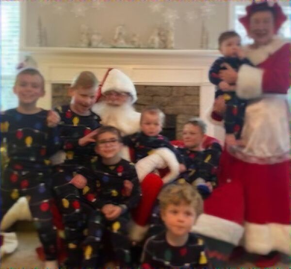 Boys in matching pajamas with Santa and Mrs. Claus by the fireplace