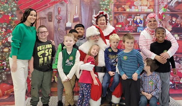 Children and teachers with Santa and Mrs. Claus in front of a Christmas backdrop