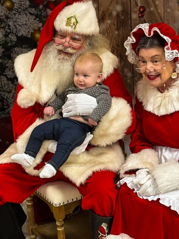 Baby on Santa Truette's lap with Mrs. Claus Nancy beside them