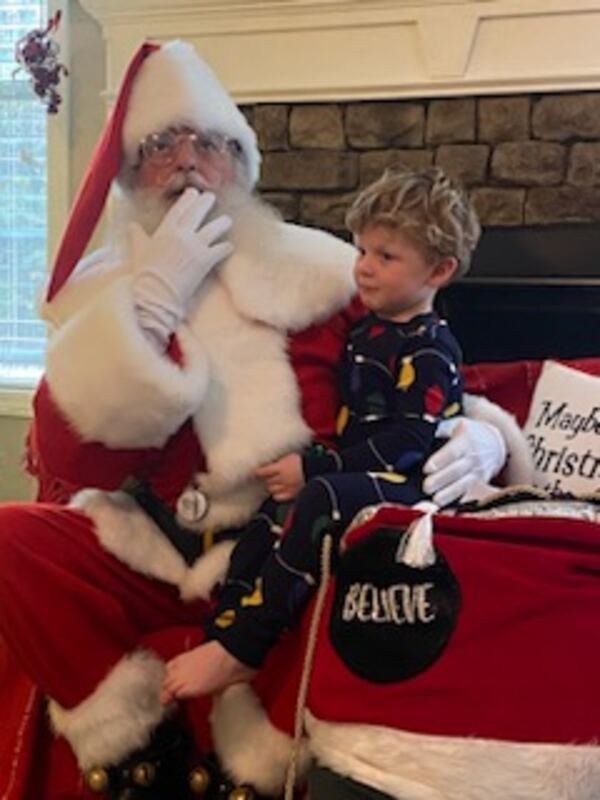 Little boy in pajamas with Santa Truette and a Believe sign