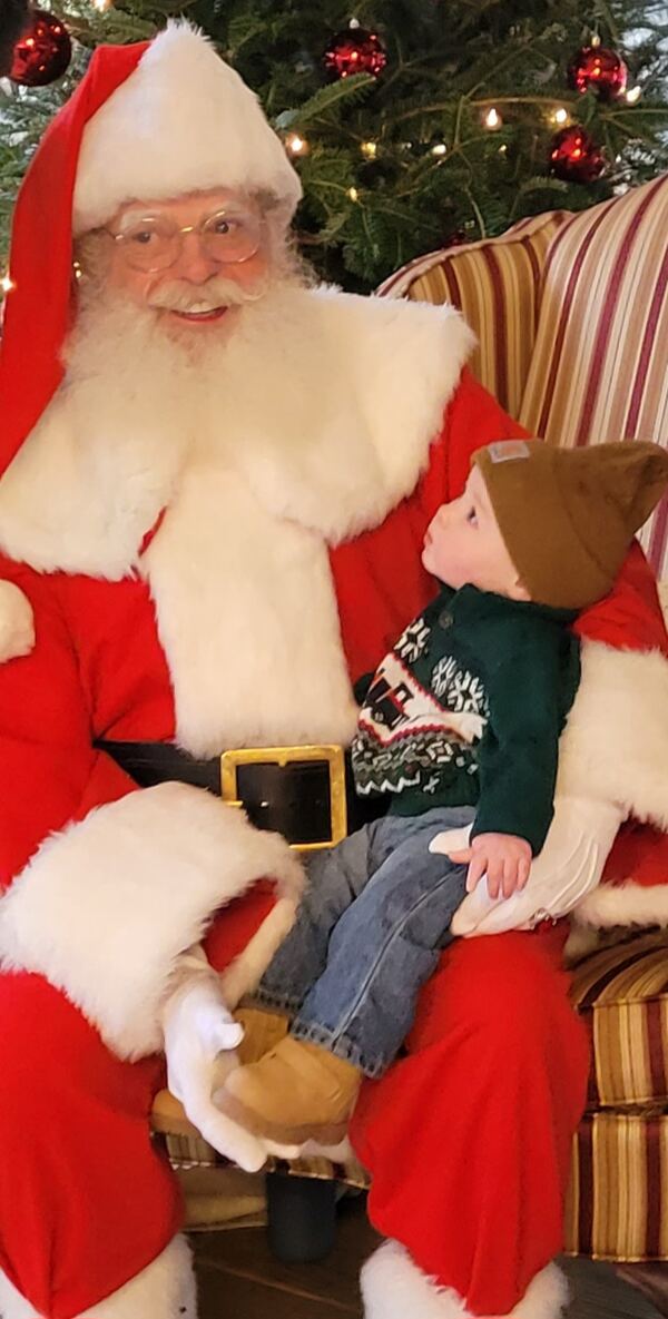 Toddler in a knit hat on Santa's knee by the tree