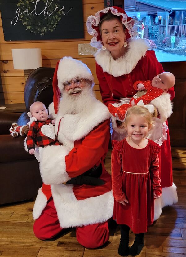 Mrs. Claus holding a baby with Santa and a little girl in a red dress