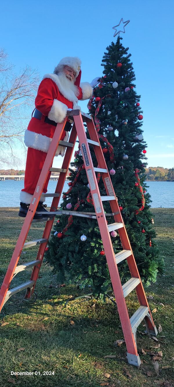 Santa Truette on a ladder decorating a Christmas tree