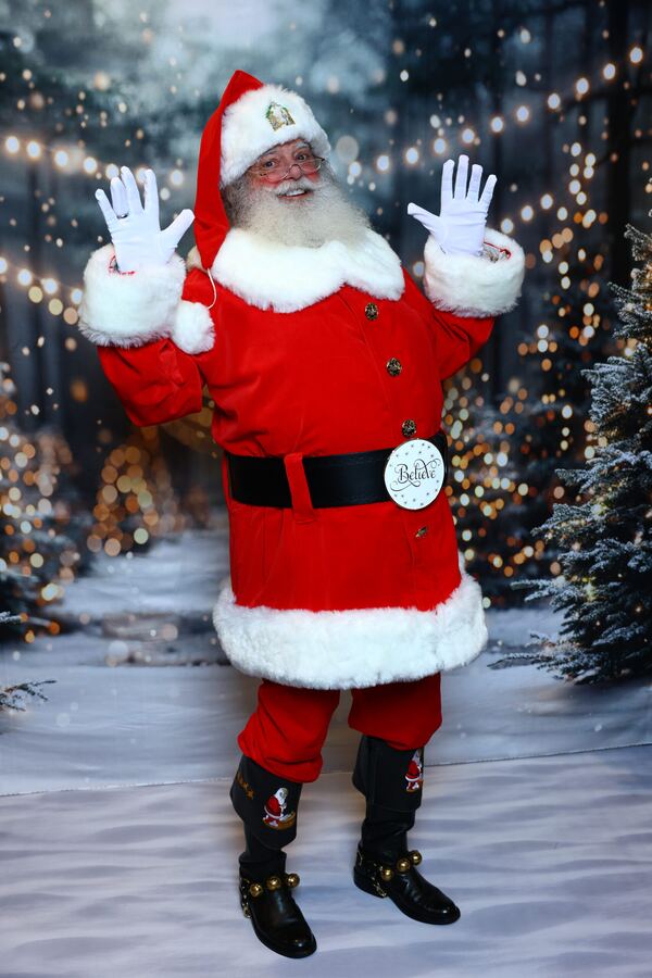 Santa Truette waving in front of a snowy, twinkle-lit forest