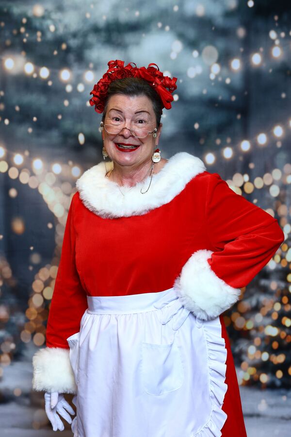 Mrs. Claus Nancy in her red dress and white apron, hand on hip