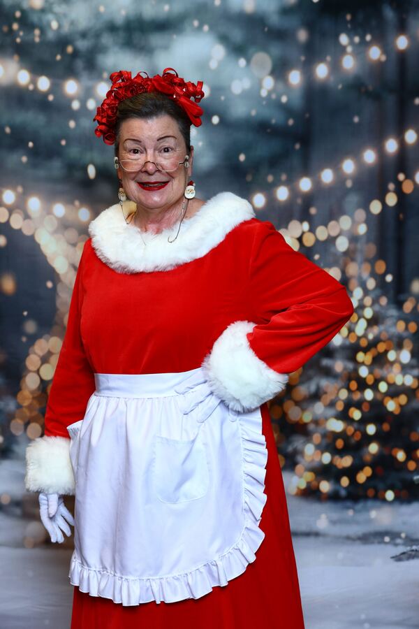 Mrs. Claus Nancy in red dress and apron against a snowy backdrop