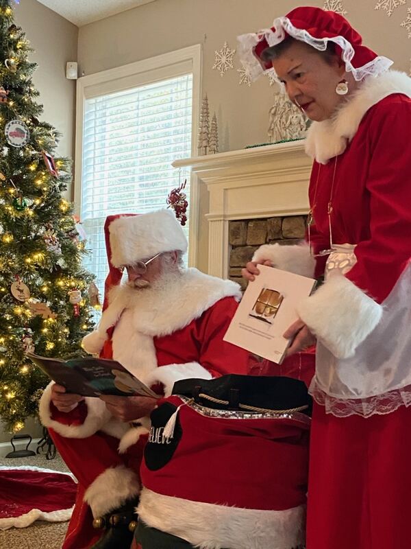 Mrs. Claus Nancy handing Santa Truette a letter by the fireplace