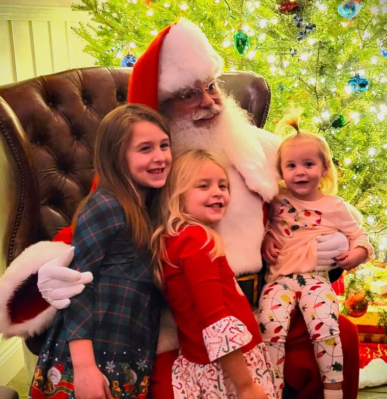 Three sisters smiling with Santa in front of a Christmas tree